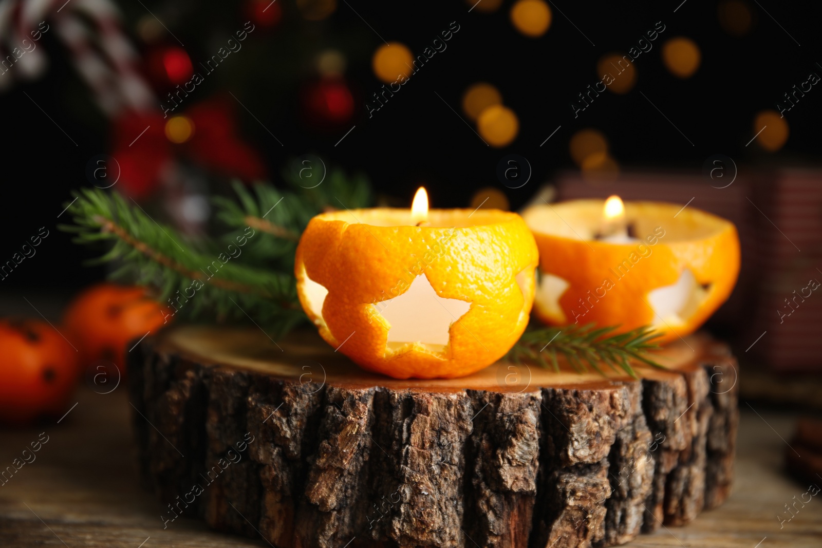 Photo of Burning candles in tangerine peels as holders on stump, closeup
