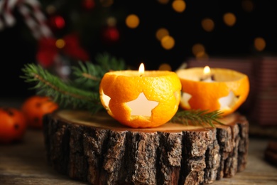 Photo of Burning candles in tangerine peels as holders on stump, closeup