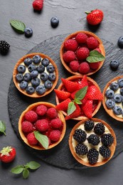 Tartlets with different fresh berries on black table, flat lay. Delicious dessert