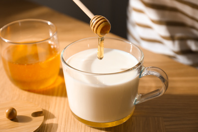 Photo of Adding honey to milk at wooden table, closeup