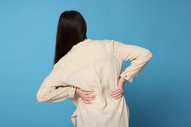 Photo of Young woman suffering from pain in back on light blue background. Arthritis symptoms