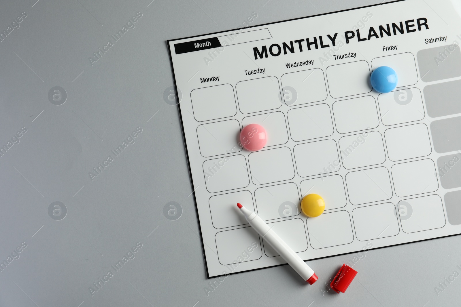 Photo of Timetable. Planner with bright magnets and red felt pen on grey table, top view. Space for text