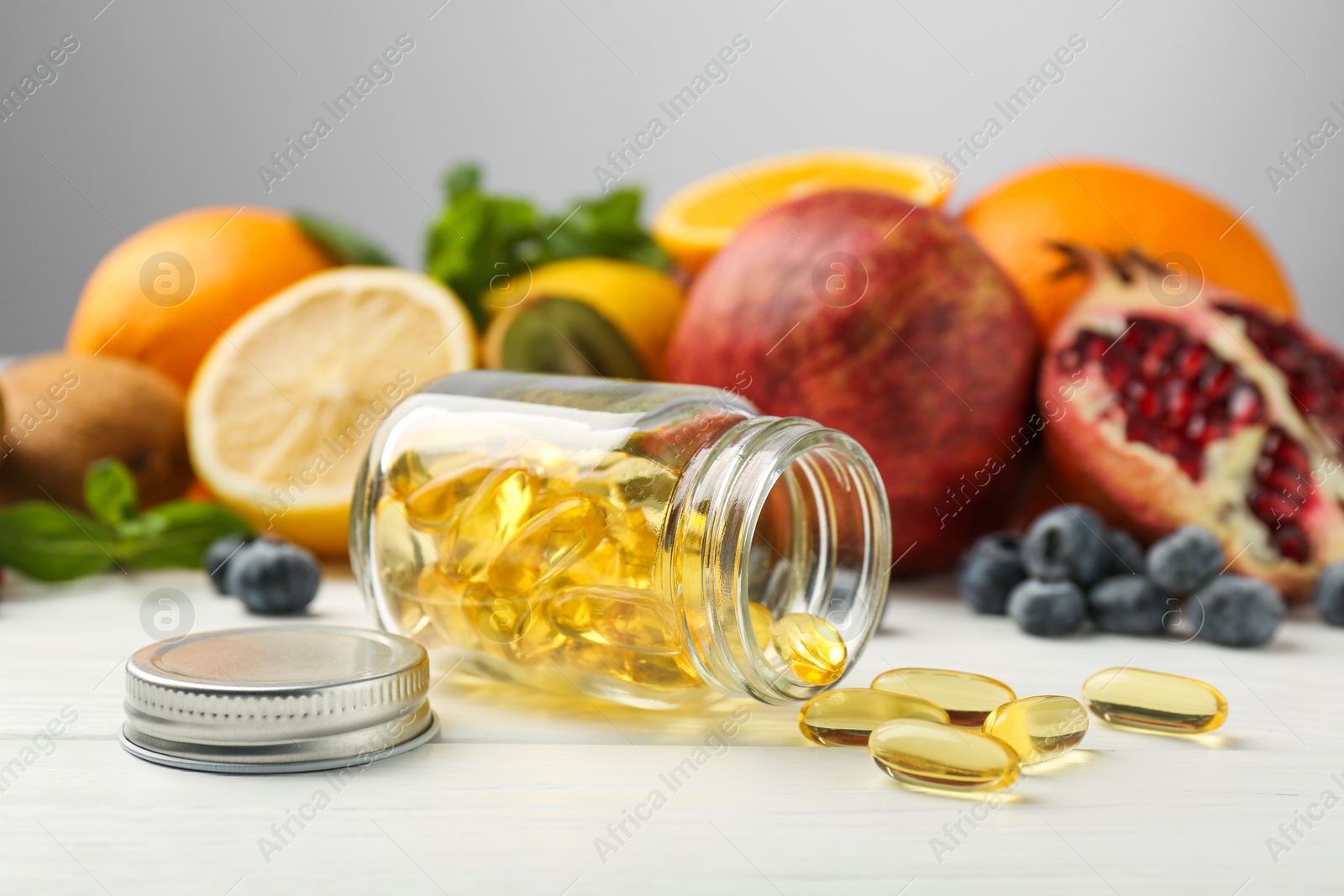 Photo of Vitamin pills, bottle and fresh fruits on white wooden table