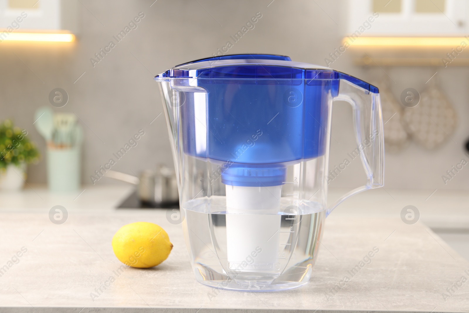 Photo of Water filter jug and lemon on light grey table in kitchen