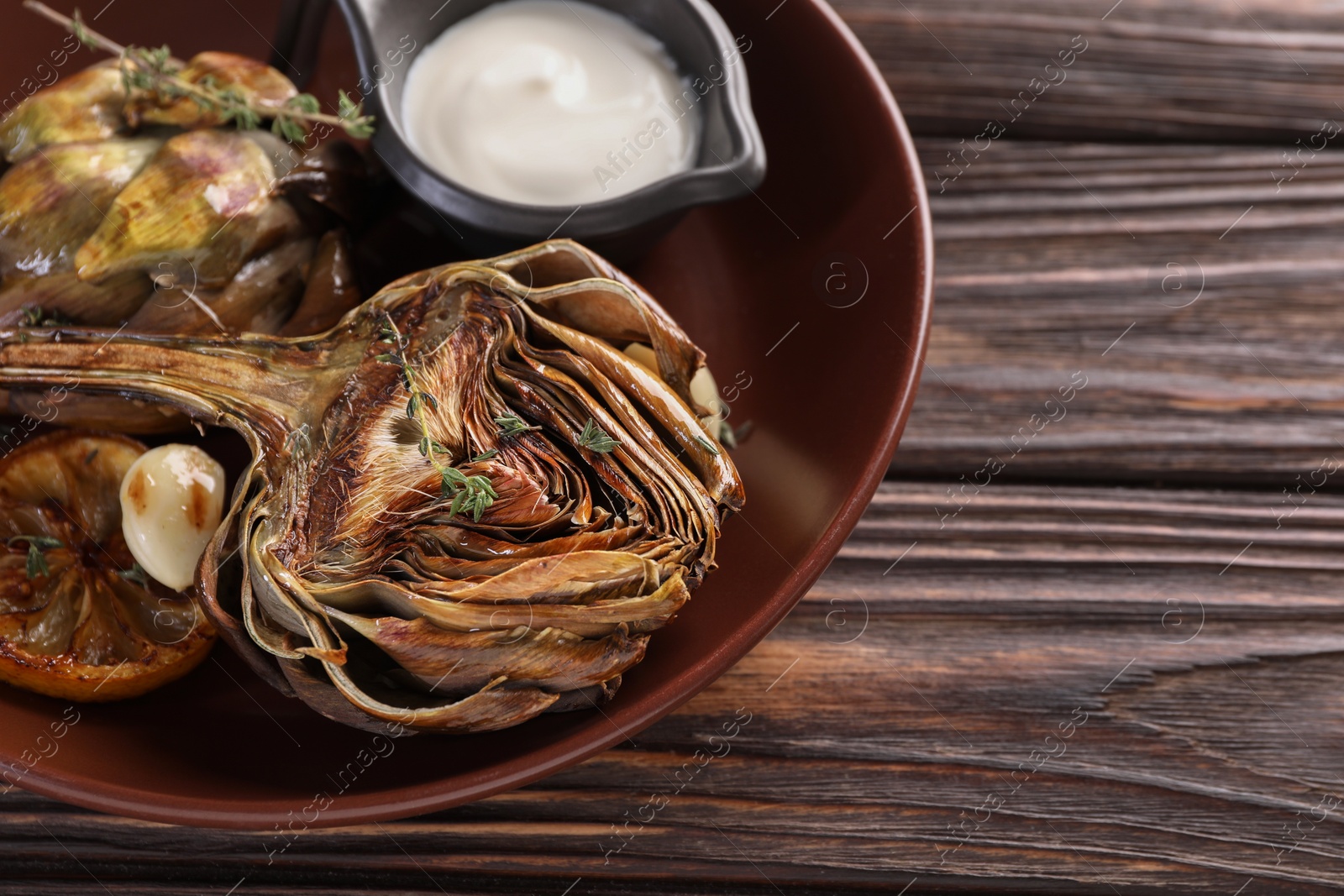Photo of Tasty grilled artichoke and sauce in bowl on wooden table, closeup. Space for text
