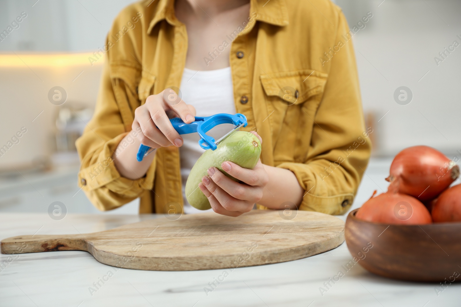 Photo of Woman peeling zucchini at table in kitchen, closeup. Preparing vegetable