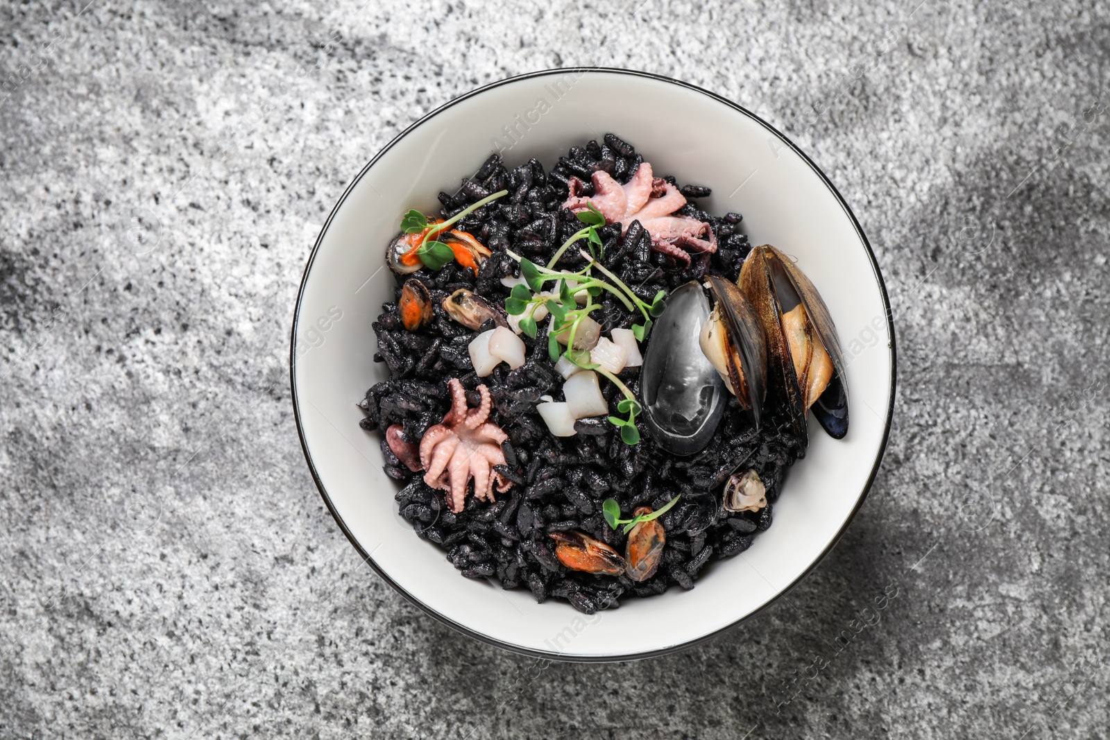 Photo of Delicious black risotto with seafood in bowl on light grey table, top view