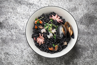 Photo of Delicious black risotto with seafood in bowl on light grey table, top view