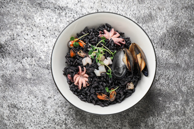 Delicious black risotto with seafood in bowl on light grey table, top view