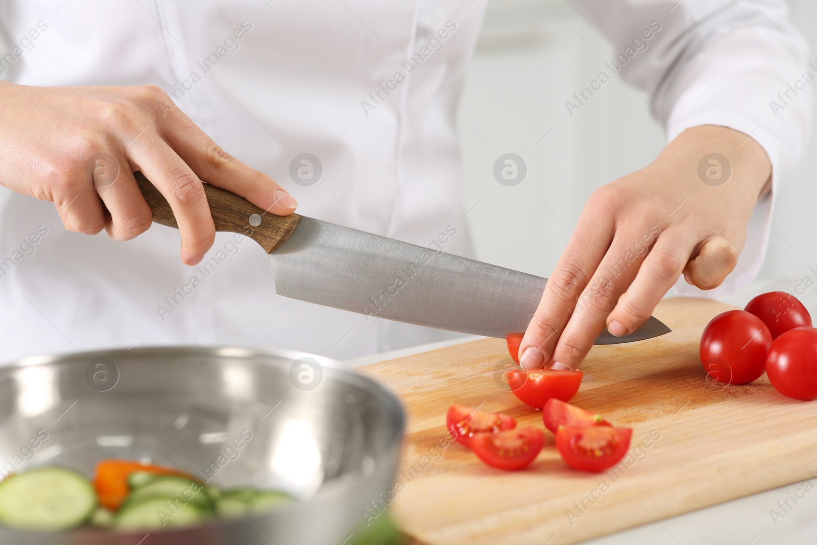 Photo of Professional chef cutting fresh tomatoes at white marble table in kitchen, closeup