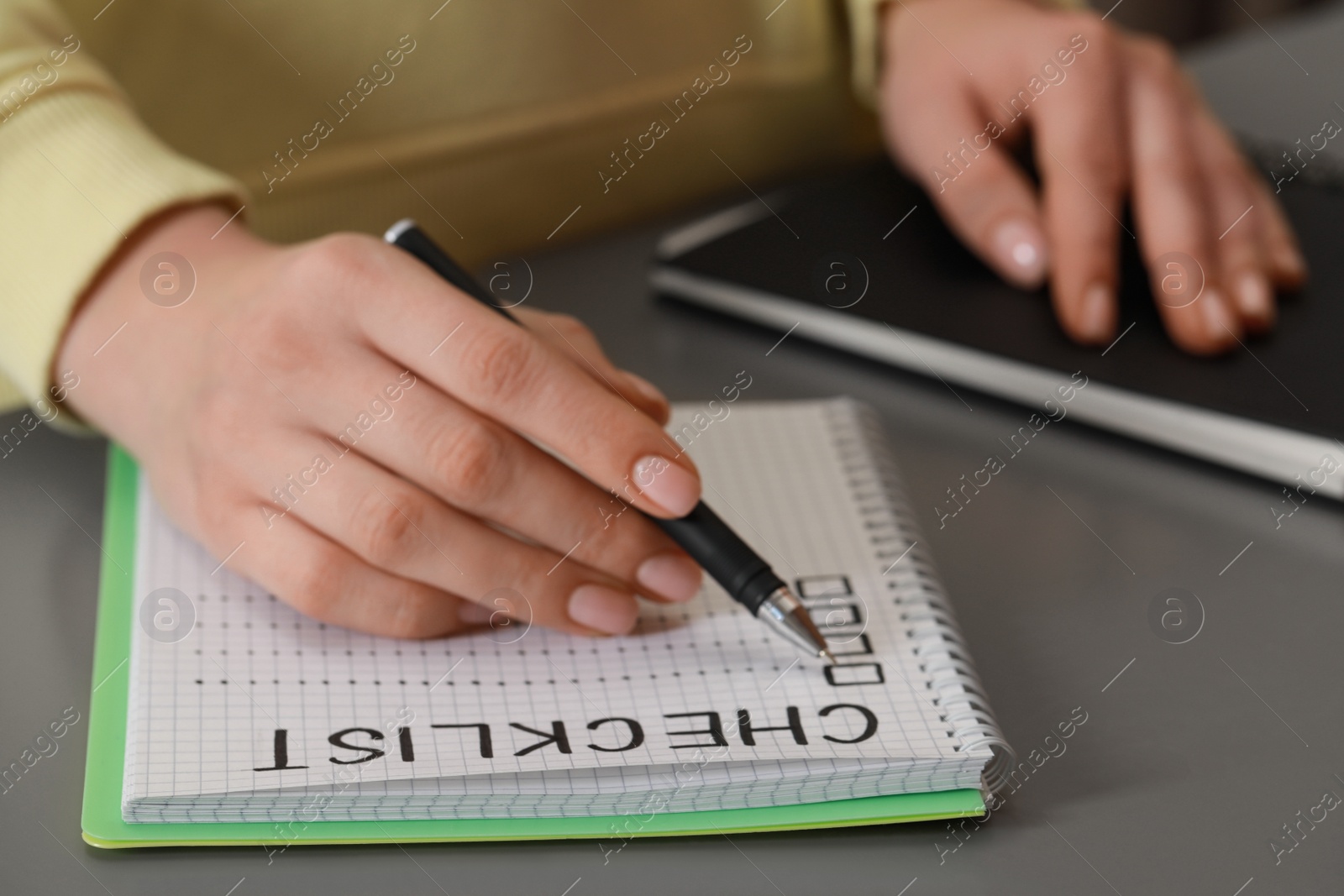 Photo of Woman filling Checklist with pen at grey table, closeup