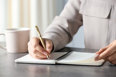 Photo of Woman writing in notebook with pen at grey table indoors, closeup
