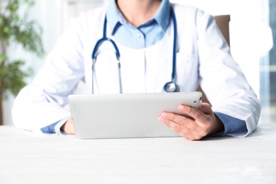 Female doctor with modern tablet sitting at table indoors, closeup