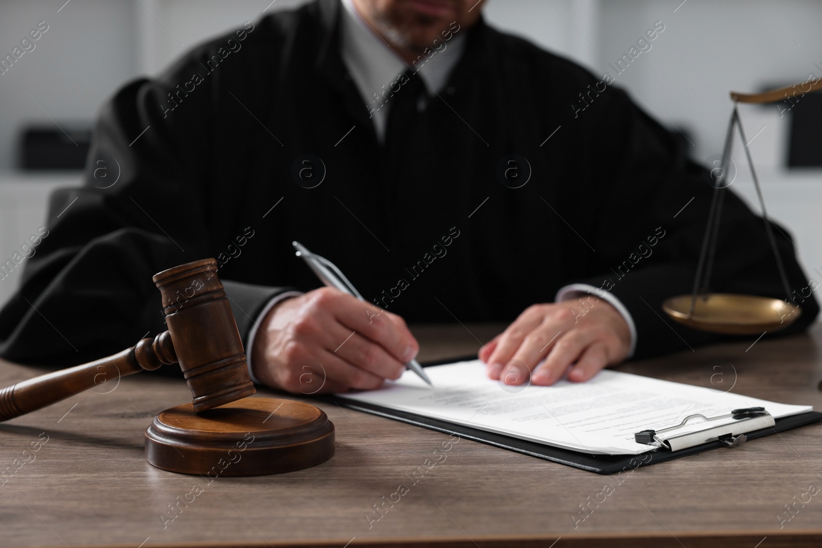 Photo of Judge with gavel writing in papers at wooden table indoors, closeup