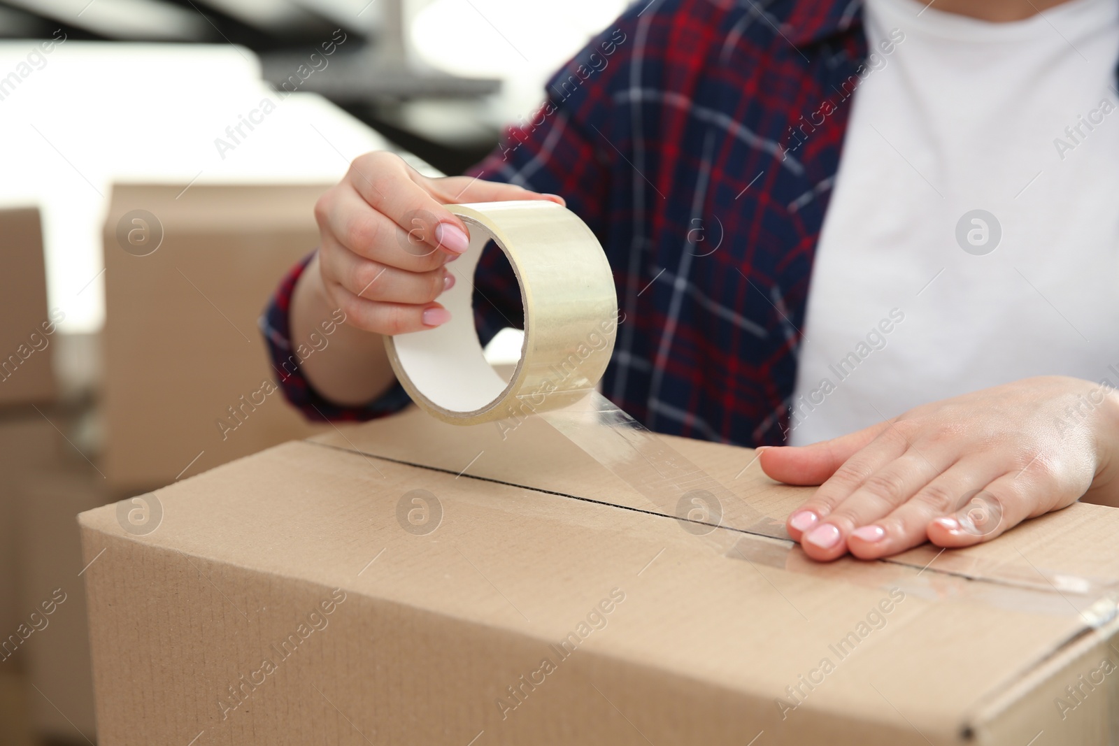 Photo of Woman taping cardboard box indoors, closeup. Moving day