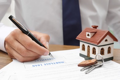 Image of Mortgage loan agreement Man with document, closeup. Model of house and keys on table