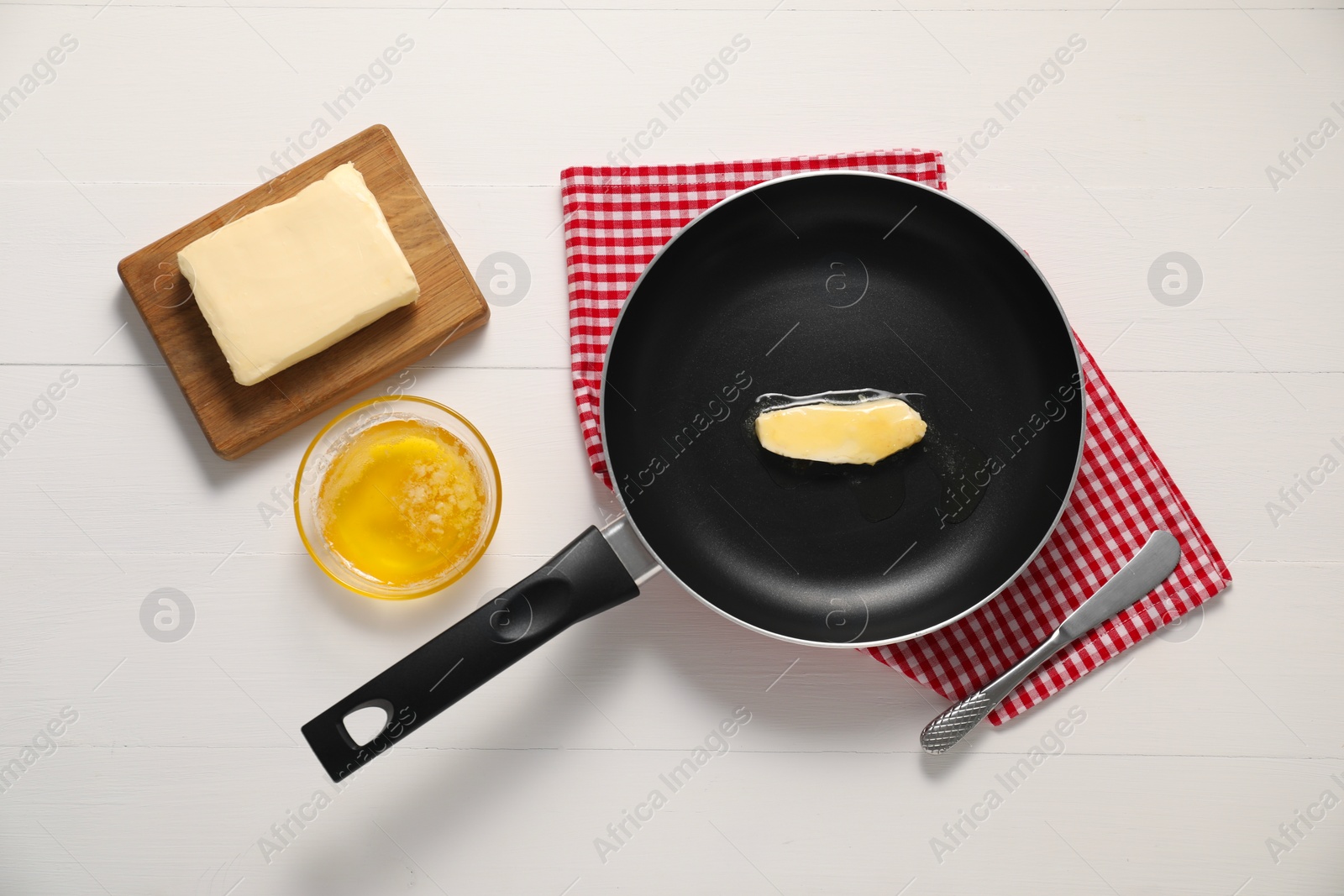 Photo of Melting butter in frying pan and knife on white wooden table, flat lay