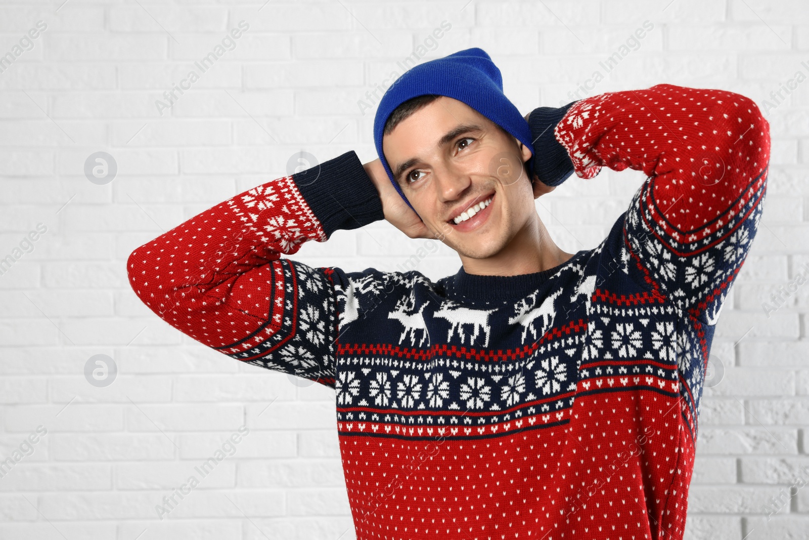 Photo of Portrait of young man in Christmas sweater and hat near white brick wall