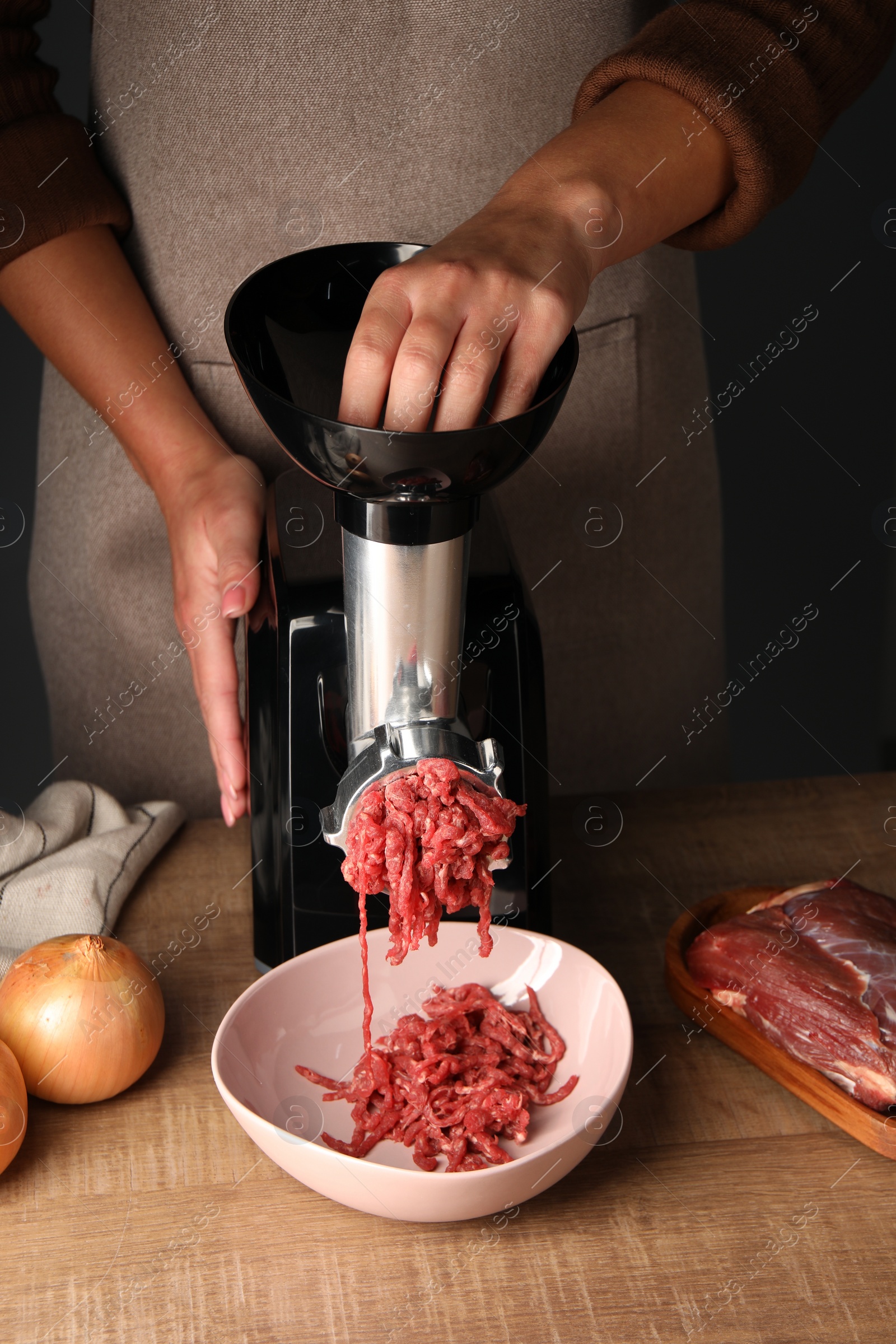Photo of Woman making beef mince with electric meat grinder at wooden table, closeup