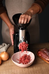 Woman making beef mince with electric meat grinder at wooden table, closeup