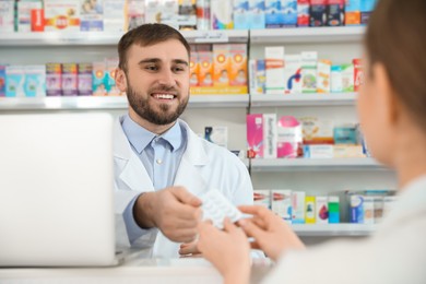 Professional pharmacist giving pills to customer in modern drugstore