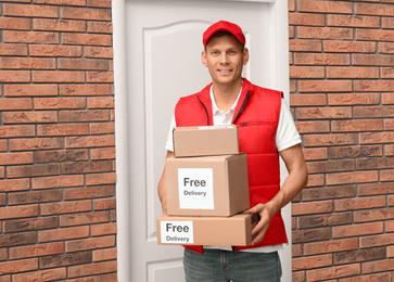 Photo of Courier holding parcels with stickers Free Delivery indoors