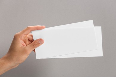 Man holding flyers on grey background, closeup. Mockup for design