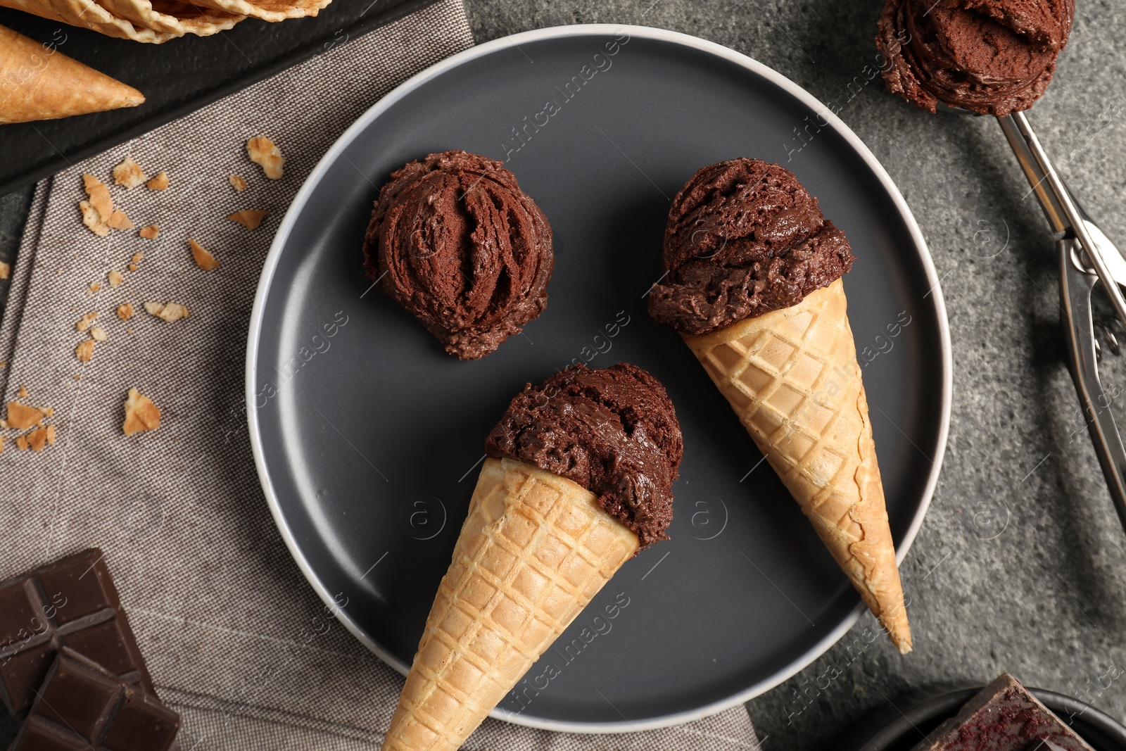 Photo of Chocolate ice cream scoops in wafer cones on gray textured table, flat lay
