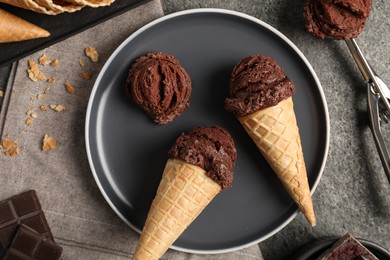 Photo of Chocolate ice cream scoops in wafer cones on gray textured table, flat lay