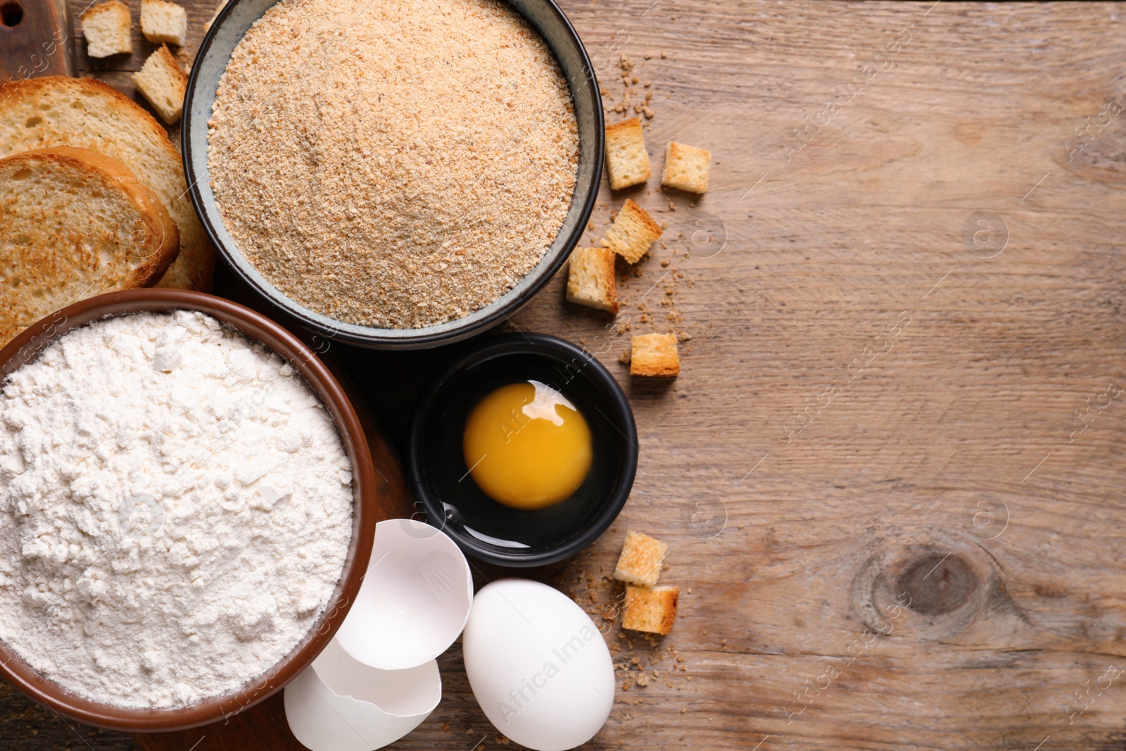 Photo of Fresh breadcrumbs, flour and eggs on wooden table, flat lay. Space for text