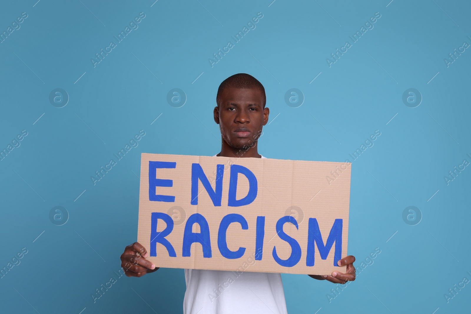 Photo of African American man holding sign with phrase End Racism on light blue background