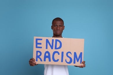 Photo of African American man holding sign with phrase End Racism on light blue background