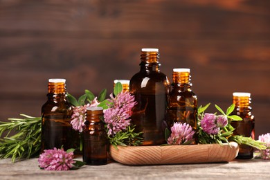 Bottles with essential oils, clover and rosemary on wooden table