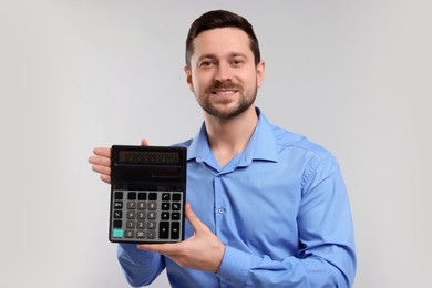 Photo of Happy accountant showing calculator on light grey background