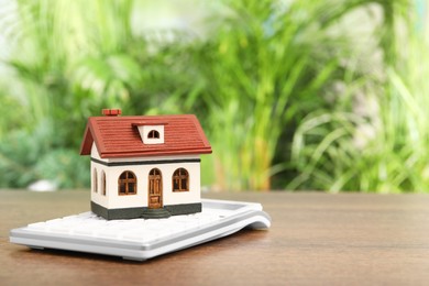 Photo of Mortgage concept. House model and calculator on wooden table against blurred green background, closeup with space for text