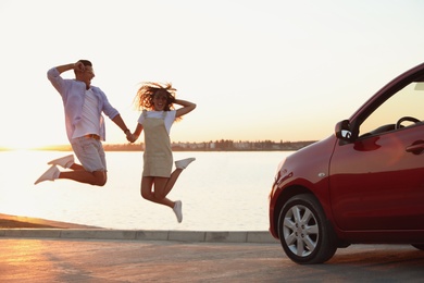 Photo of Happy couple jumping near car outdoors at sunset. Summer trip