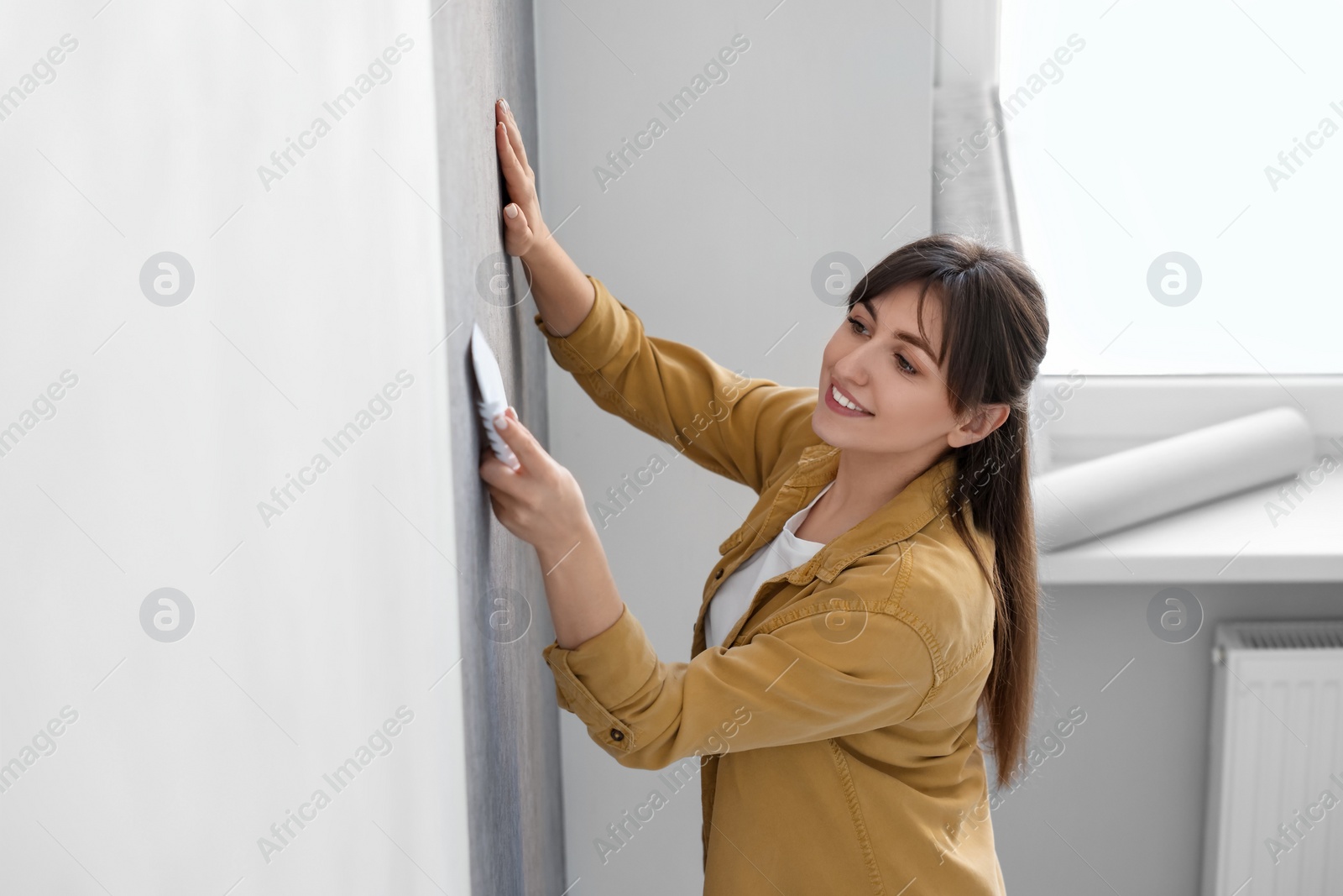 Photo of Woman smoothing stylish gray wallpaper in room