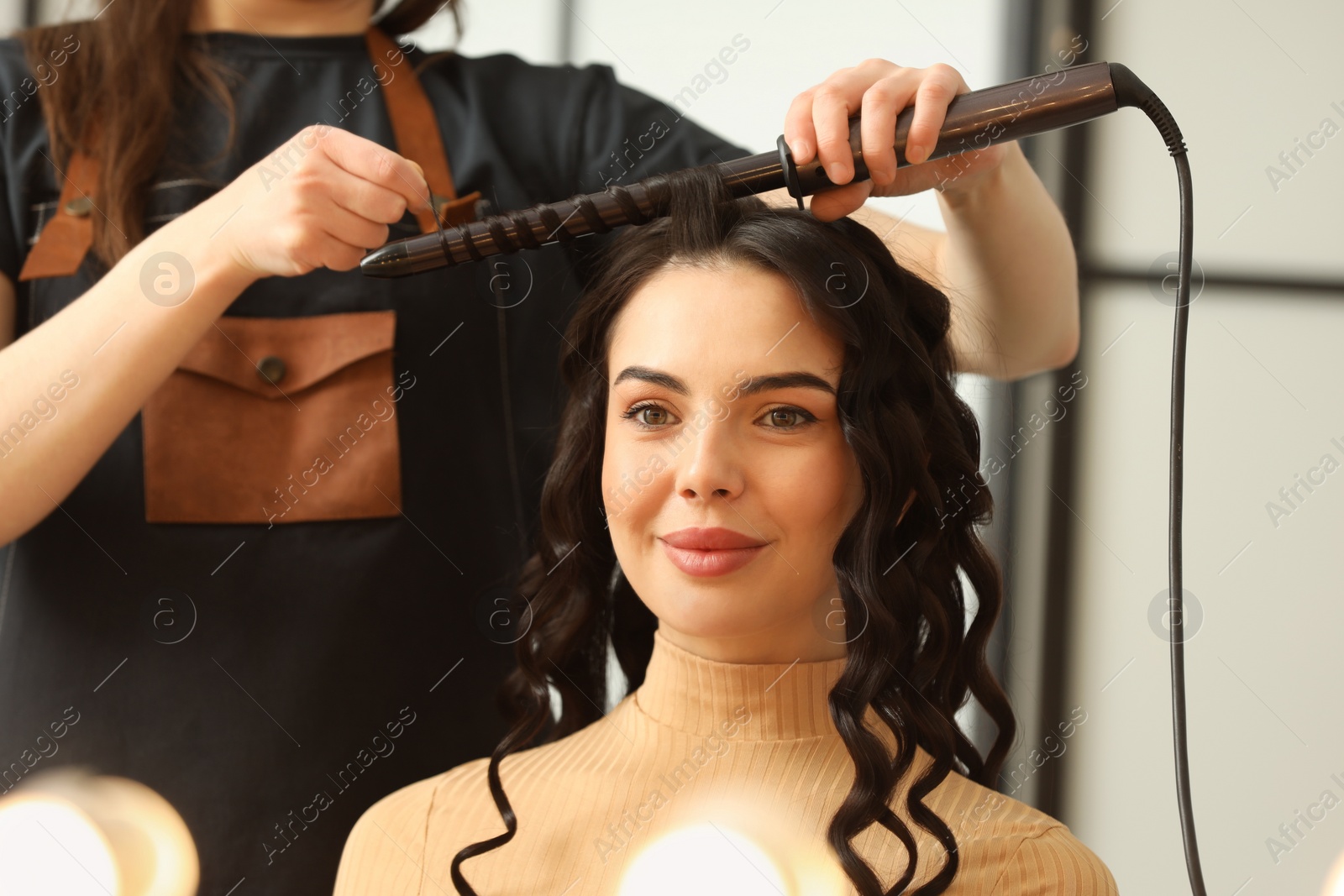 Photo of Hair styling. Hairdresser curling woman's hair in salon, closeup