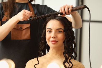 Photo of Hair styling. Hairdresser curling woman's hair in salon, closeup