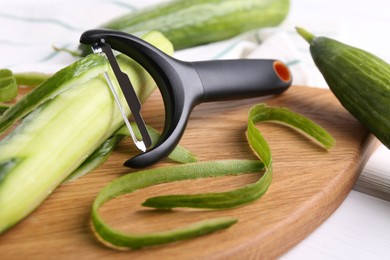 Photo of Fresh cucumbers, peels and peeler on white table, closeup