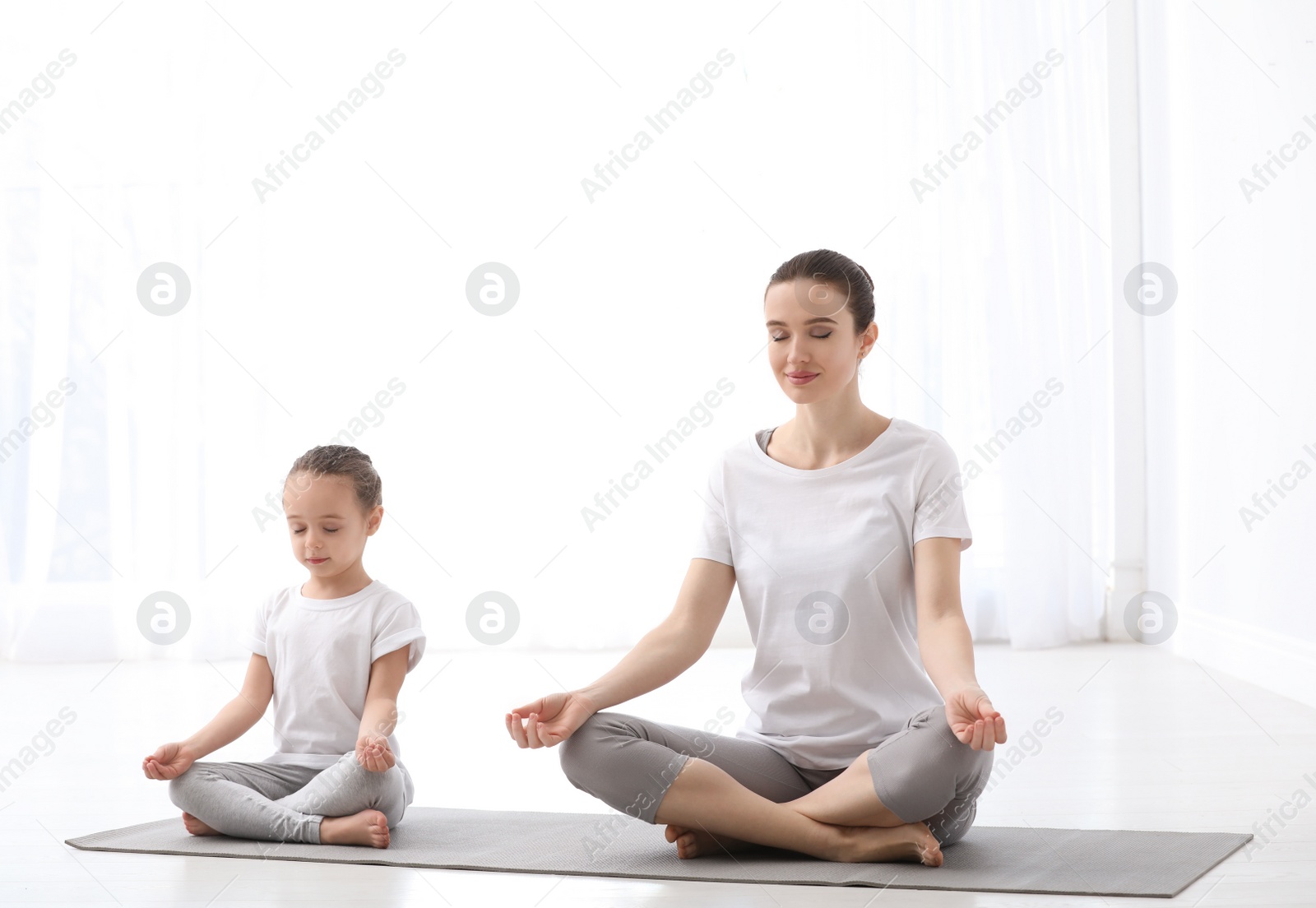 Photo of Young mother with little daughter practicing yoga at home