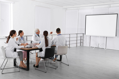 Photo of Team of doctors using video projector during conference indoors