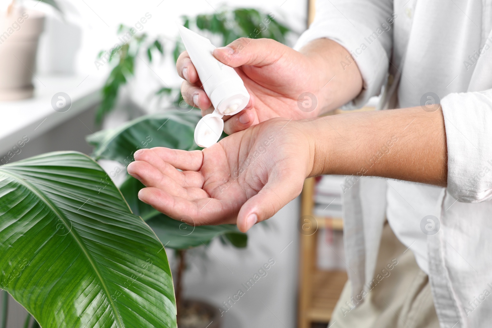 Photo of Man applying hand cream from tube at home, closeup