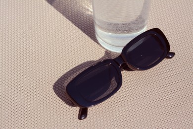 Photo of Stylish sunglasses and glass of water on grey surface, closeup