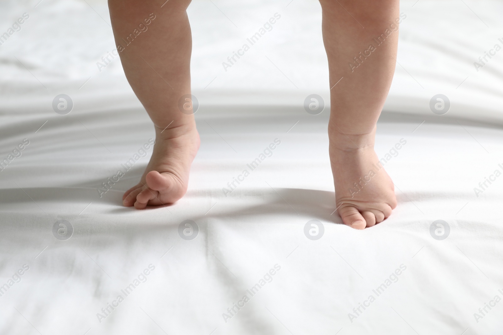 Photo of Cute little baby standing on white bed sheet, closeup