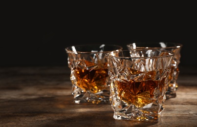 Golden whiskey in glass with ice cubes on table. Space for text