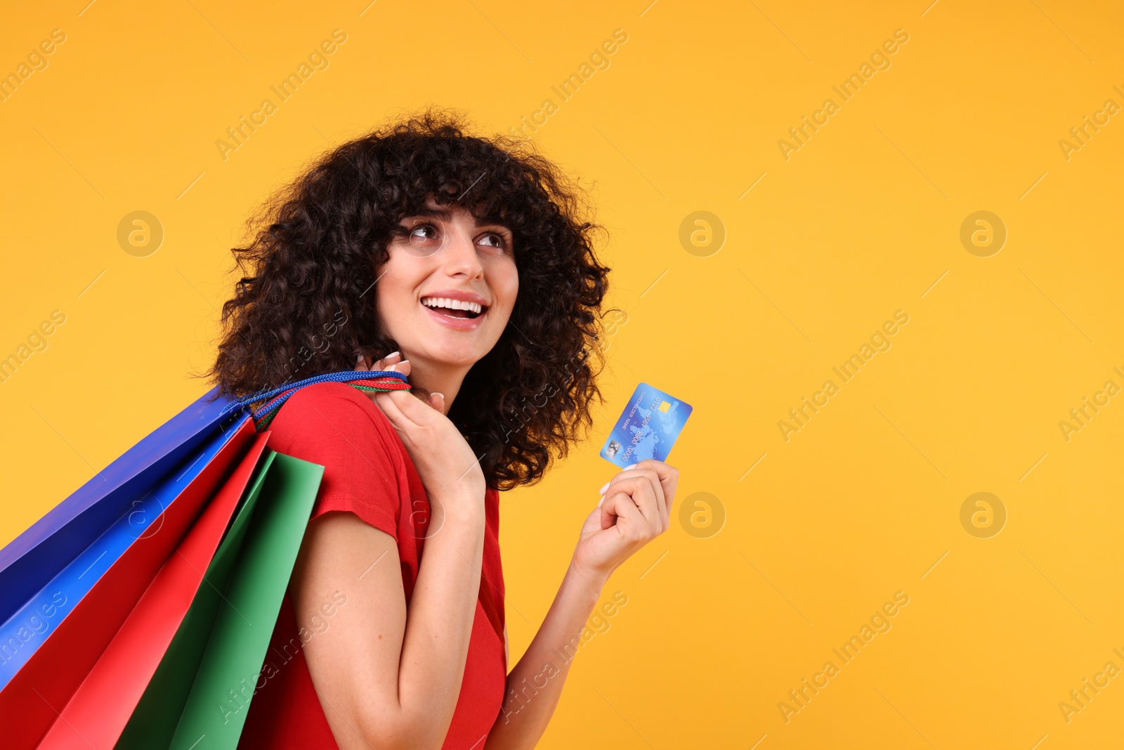 Photo of Happy young woman with shopping bags and credit card on yellow background