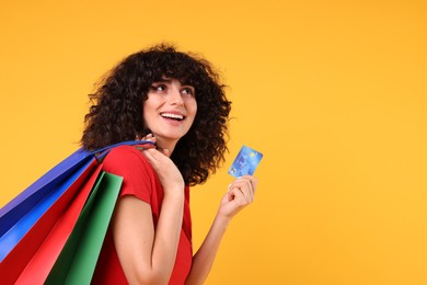 Happy young woman with shopping bags and credit card on yellow background