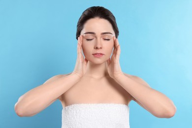 Photo of Young woman massaging her face on turquoise background