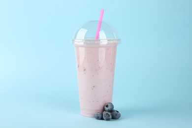 Plastic cup of tasty smoothie and fresh blueberry on light blue background